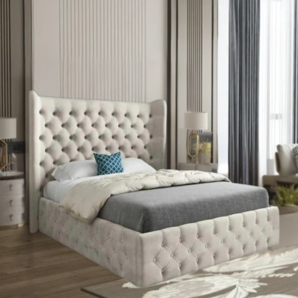 Modern bedroom with a tufted beige bed, blue pillow, lamp on bedside table, and tall drapes.