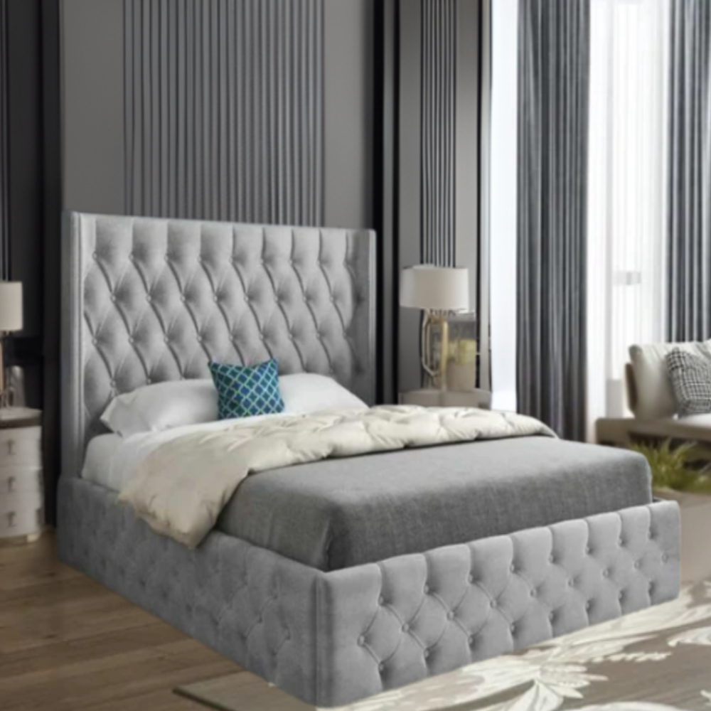 A modern bedroom with a large bed featuring a gray tufted headboard and frame, white and beige bedding, teal accent pillow, and matching nightstands with lamps.