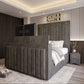 Modern bedroom with the 2025 The Zenith TV Bed featuring a gray tufted headboard, chandelier, and integrated footboard TV.