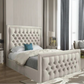 Modern bedroom with a tufted beige bed, blue pillow, lamp on bedside table, and tall drapes.