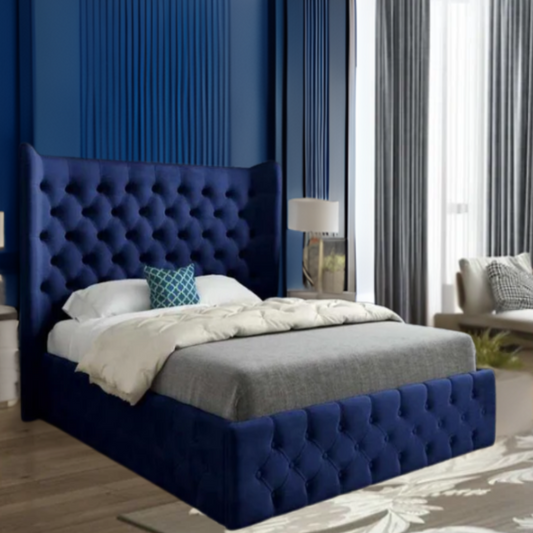 Bedroom with a deep blue tufted bed, grey bedding, and a teal cushion, set against a blue paneled wall.