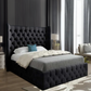 Bedroom with a dark tufted bed, large windows, and modern furnishings.