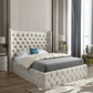 Modern bedroom with a tufted beige bed, blue pillow, lamp on bedside table, and tall drapes.