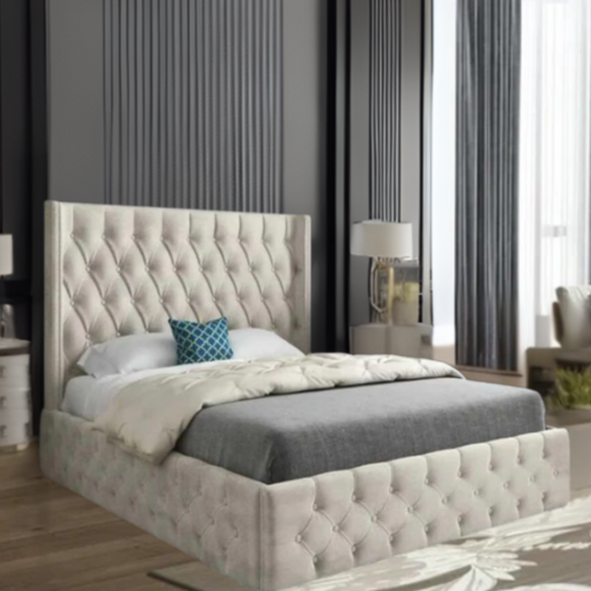 A modern bedroom featuring a large tufted bed with beige fabric, gray blanket, and teal pillow, set against dark panel walls and large window with curtains.