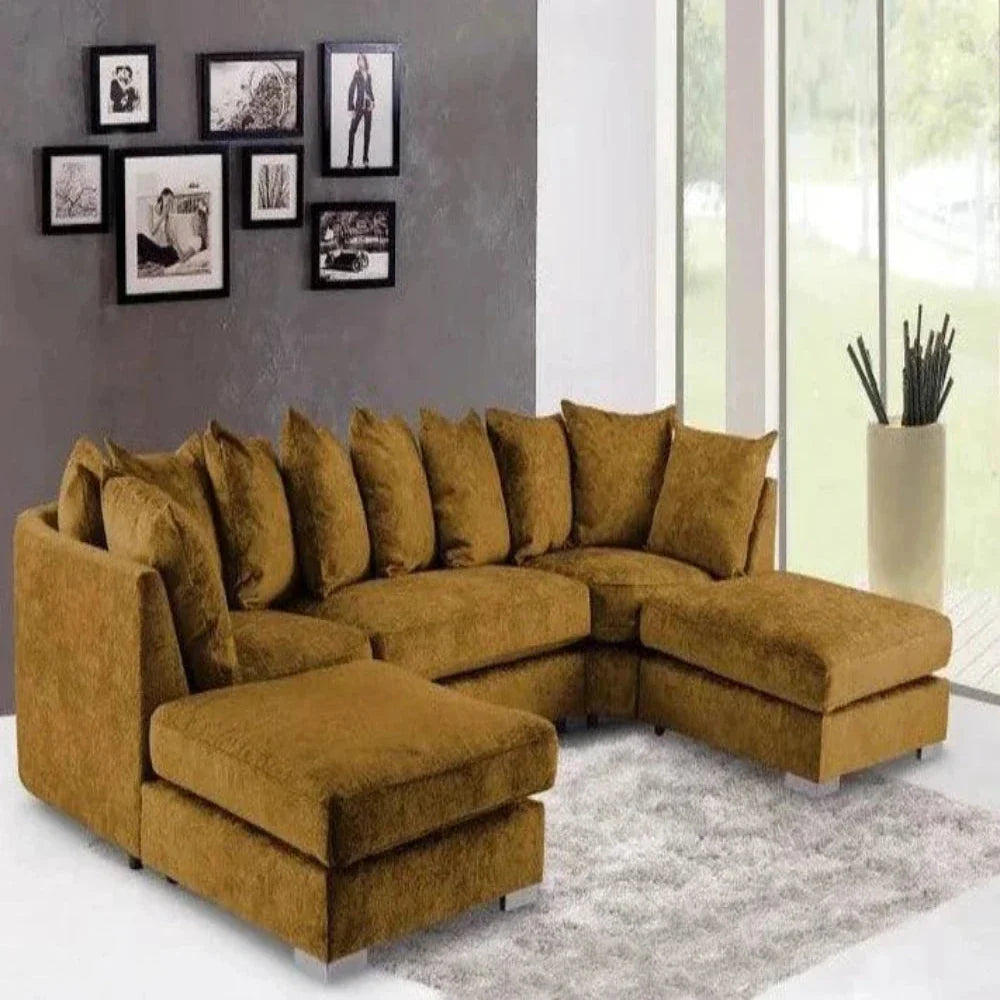 This modern living room features a U-shaped Elveden sofa in mustard-yellow fabric, accented with matching throw pillows. It sits on a light gray shag rug beneath a collage of black-and-white photographs. Floor-to-ceiling windows provide natural light and views of the outdoors, while a tall white vase with decorative sticks adds to the contemporary style.